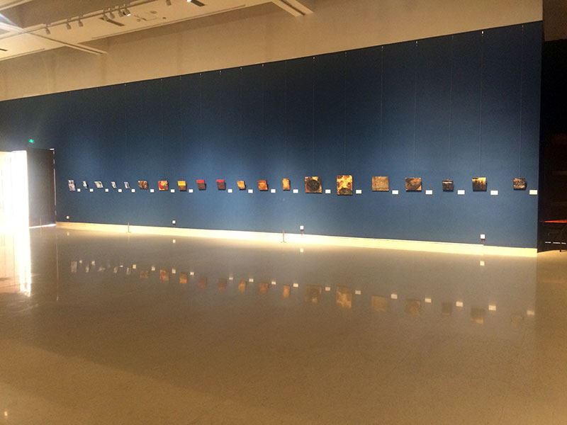Exhibition view showing a long wall lined with small-scale Nihonga works in a spacious gallery room